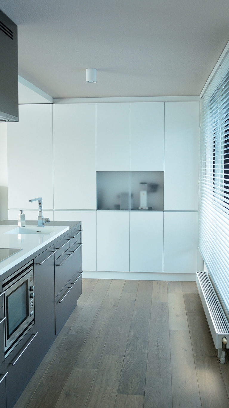 Hoge keukenkast gespoten in de twee componenten meubellak Achter matte plexiglas schuifdeuren bevinden zich verschillende keuken apparaten.